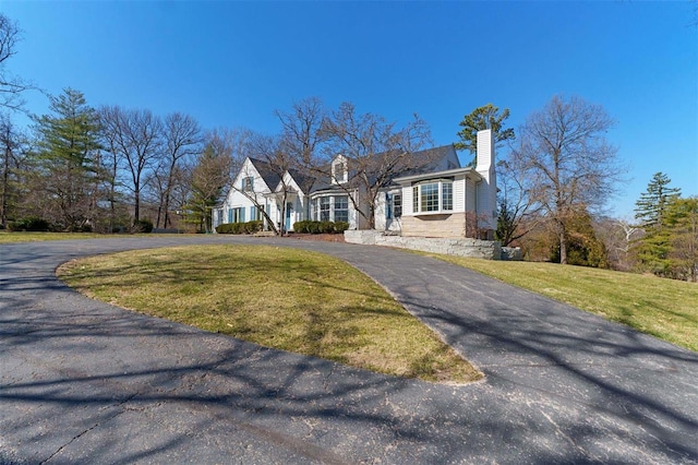 view of front of property with aphalt driveway, a front lawn, and a chimney