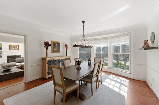 dining area with a notable chandelier, ornamental molding, a glass covered fireplace, wood finished floors, and baseboards