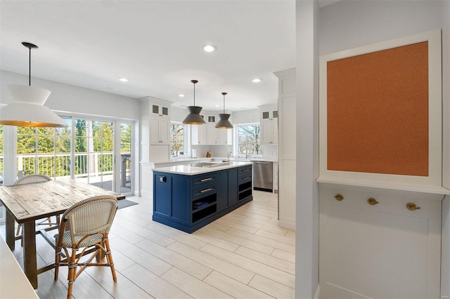 kitchen featuring blue cabinetry, light countertops, stainless steel dishwasher, glass insert cabinets, and white cabinets