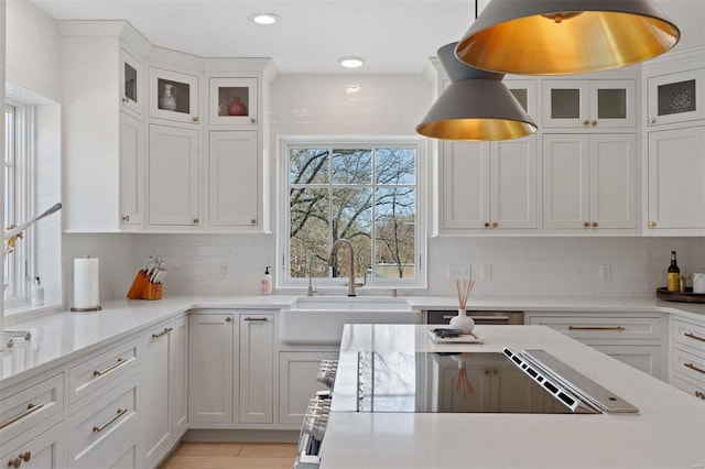 kitchen featuring pendant lighting, light countertops, decorative backsplash, white cabinets, and a sink