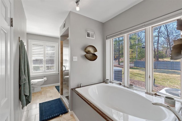 bathroom with baseboards, a garden tub, visible vents, and toilet