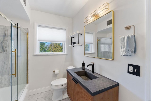 bathroom with visible vents, toilet, enclosed tub / shower combo, vanity, and baseboards