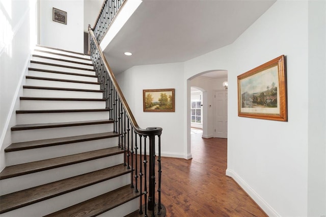 staircase with arched walkways, recessed lighting, wood finished floors, and baseboards