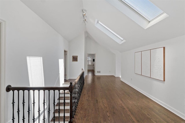 hall featuring a skylight, baseboards, wood finished floors, an upstairs landing, and high vaulted ceiling