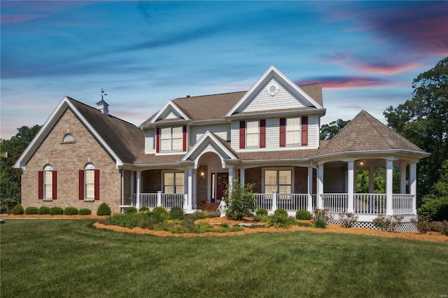 view of front of home featuring covered porch, a lawn, and brick siding