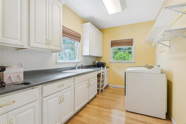 kitchen with dark countertops, washer and dryer, white cabinets, and a sink