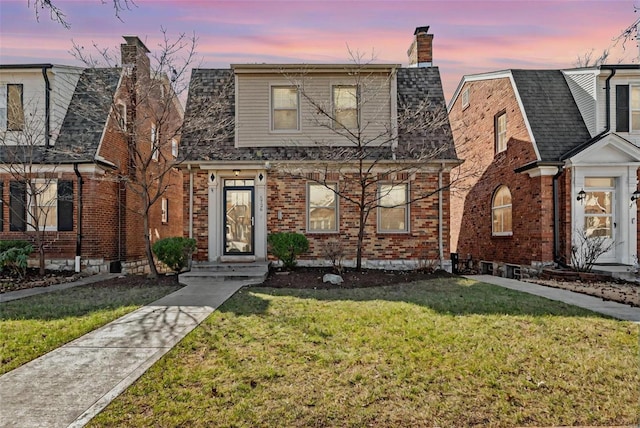 view of front of house with roof with shingles, a front yard, a chimney, and brick siding