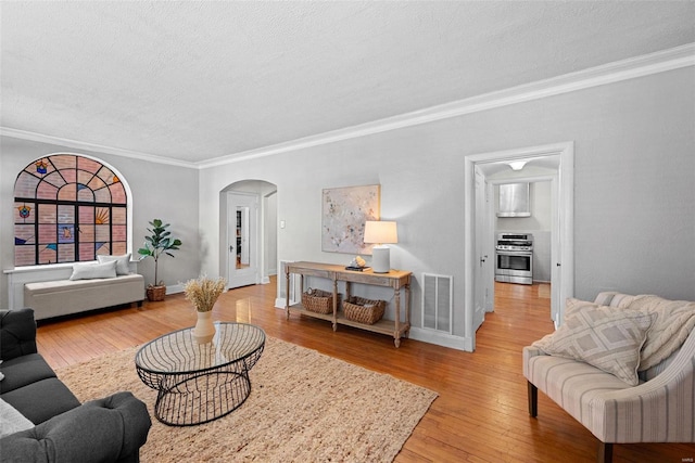 living room with ornamental molding, light wood-type flooring, visible vents, and arched walkways