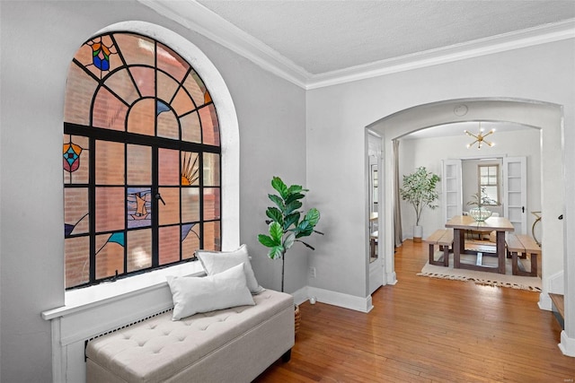 living area with a chandelier, arched walkways, wood finished floors, baseboards, and ornamental molding