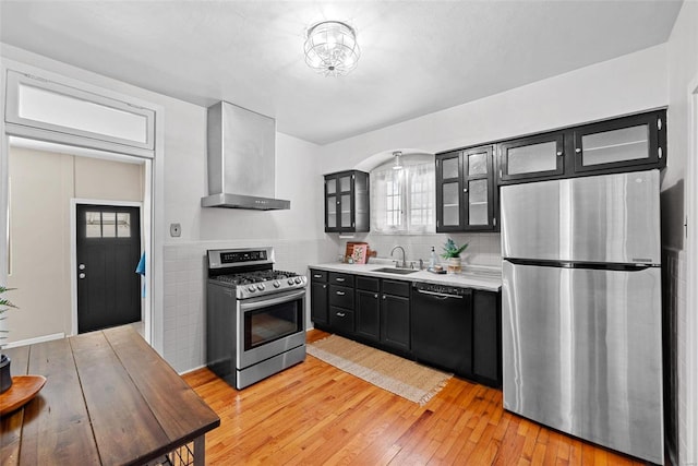 kitchen featuring dark cabinets, a sink, light countertops, appliances with stainless steel finishes, and wall chimney exhaust hood