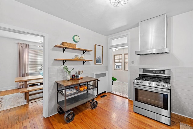 kitchen featuring light wood-type flooring, stainless steel gas stove, tile walls, and wall chimney exhaust hood