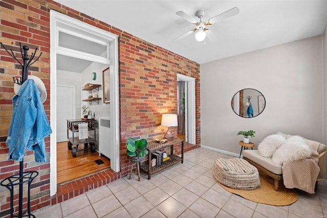 sitting room featuring baseboards, brick wall, a ceiling fan, and tile patterned floors