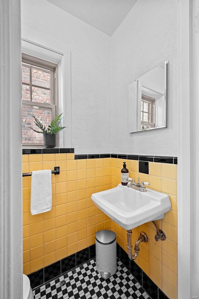 half bathroom with wainscoting, a sink, tile walls, and tile patterned floors