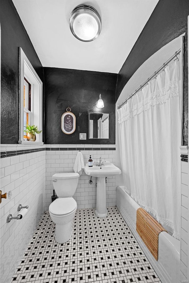 bathroom with toilet, shower / tub combo, tile walls, wainscoting, and tile patterned floors