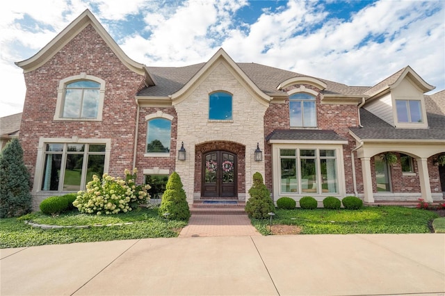 view of front of home with french doors, roof with shingles, and brick siding