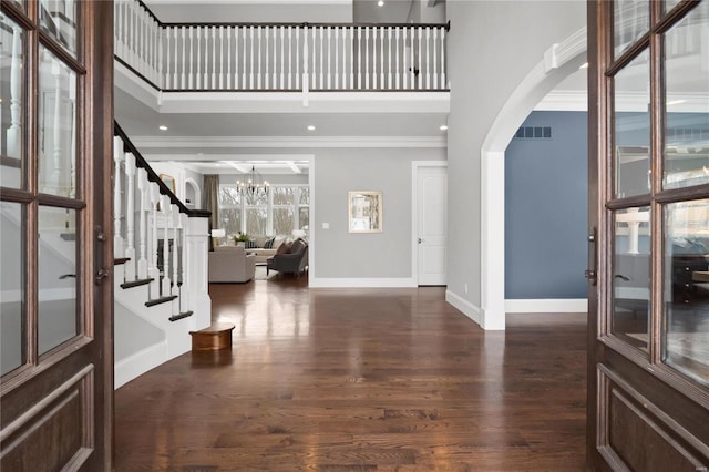 foyer entrance featuring visible vents, arched walkways, a towering ceiling, dark wood-type flooring, and crown molding