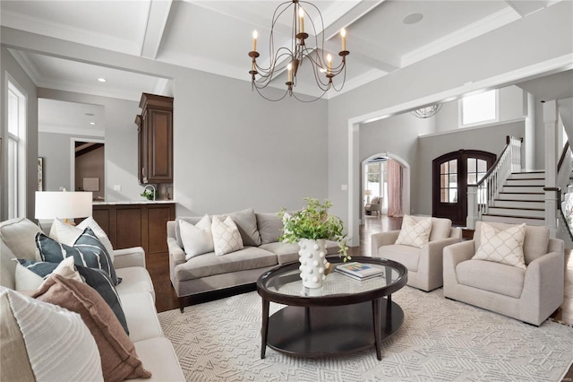 living room featuring a chandelier, stairway, light wood-type flooring, beam ceiling, and crown molding