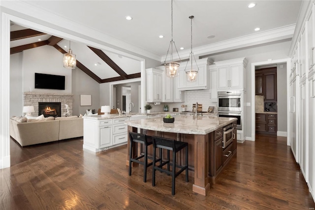 kitchen featuring open floor plan, stainless steel double oven, a kitchen bar, and a center island with sink