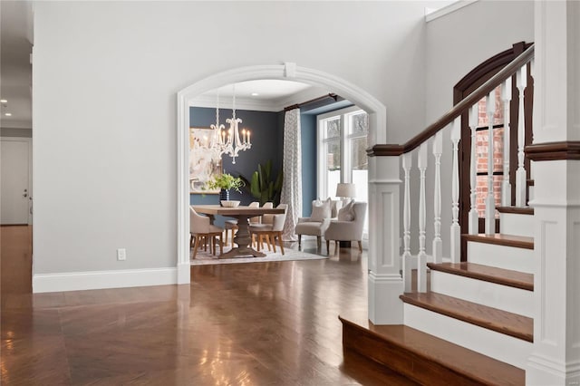 foyer featuring baseboards, arched walkways, stairway, ornamental molding, and a chandelier