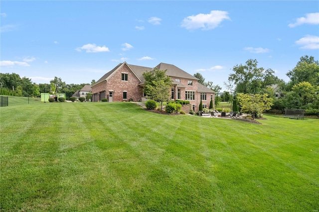 rear view of property featuring a trampoline, brick siding, a yard, and fence