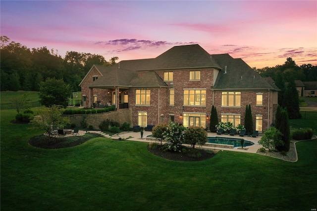 back of house at dusk with a patio, a lawn, and an outdoor pool