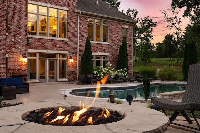 back of house at dusk with an outdoor fire pit, brick siding, a patio, and roof with shingles