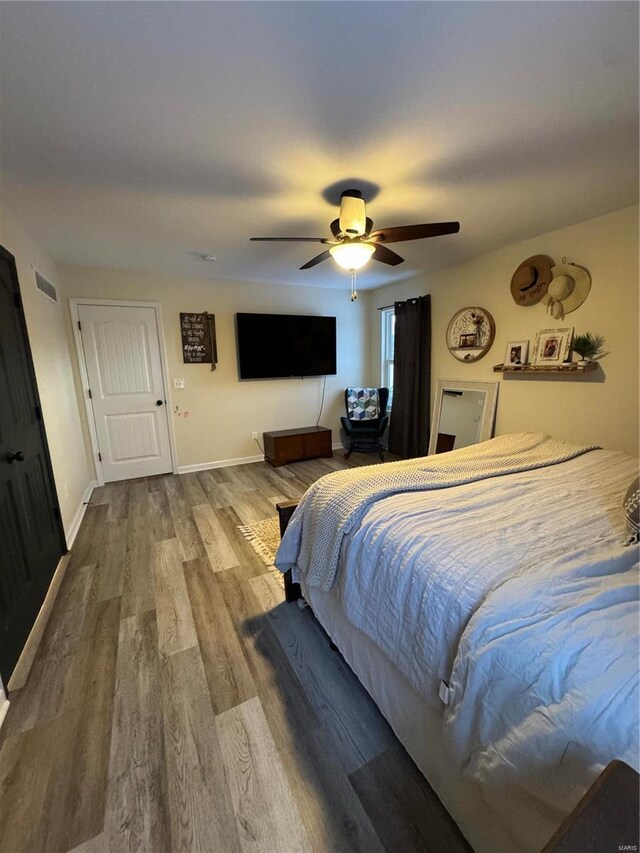 bedroom featuring a ceiling fan, wood finished floors, visible vents, and baseboards