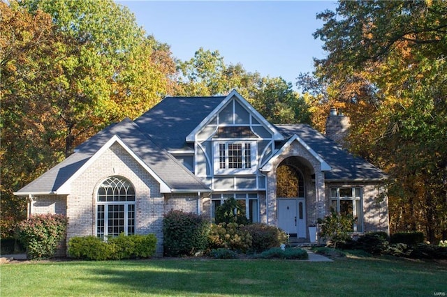 view of front of house featuring brick siding, a chimney, and a front yard