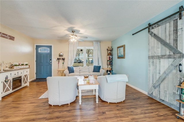 living area with a barn door, baseboards, a ceiling fan, wood finished floors, and a textured ceiling