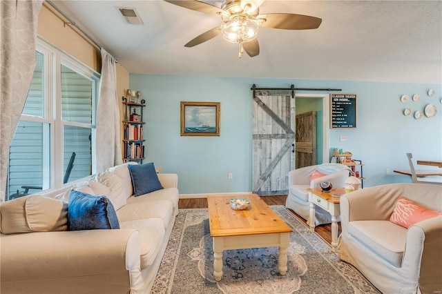 living area featuring a barn door, baseboards, visible vents, a ceiling fan, and wood finished floors