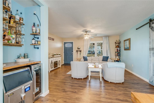 living area featuring a textured ceiling, a barn door, beverage cooler, wood finished floors, and a dry bar