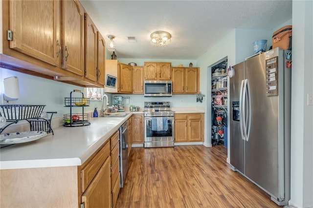 kitchen with a textured ceiling, light wood-style flooring, a sink, light countertops, and appliances with stainless steel finishes