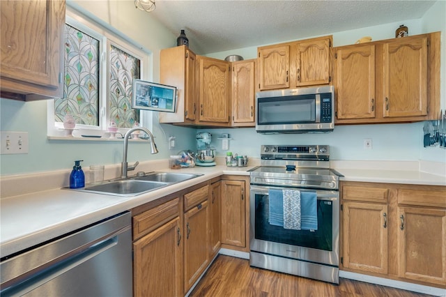 kitchen featuring appliances with stainless steel finishes, wood finished floors, light countertops, a textured ceiling, and a sink