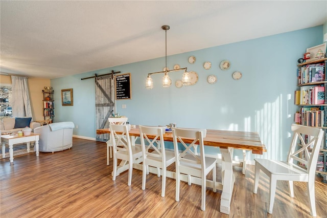 dining room with a barn door, a textured ceiling, baseboards, and wood finished floors