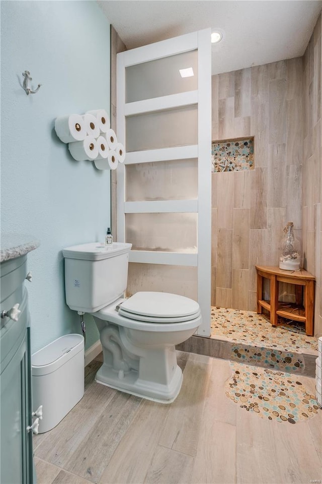 bathroom with toilet, a tile shower, and wood finished floors