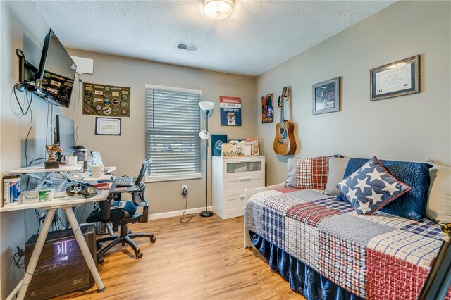 bedroom with light wood-type flooring, visible vents, a textured ceiling, and baseboards