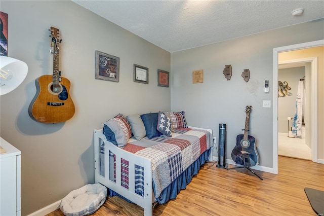 bedroom with a textured ceiling, wood finished floors, and baseboards