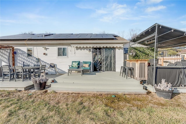 rear view of house featuring outdoor dining space, fence, a wooden deck, and roof mounted solar panels