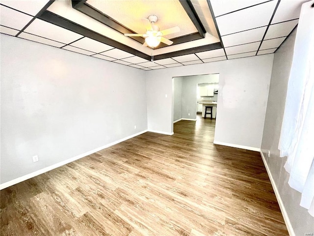 unfurnished room with baseboards, a ceiling fan, a drop ceiling, wood finished floors, and a tray ceiling