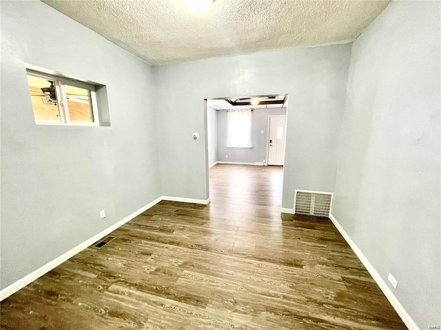 empty room with dark wood-style floors, baseboards, visible vents, and a textured ceiling