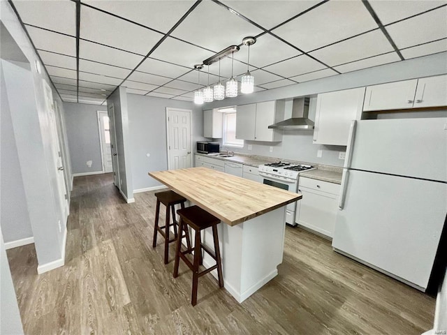 kitchen with white appliances, white cabinets, wall chimney exhaust hood, a kitchen breakfast bar, and decorative light fixtures