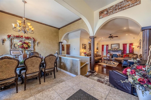 tiled dining space featuring ornamental molding, arched walkways, baseboards, and ceiling fan with notable chandelier