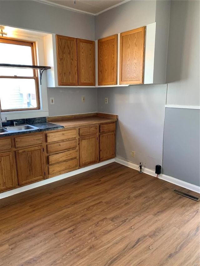 kitchen featuring dark countertops, brown cabinetry, a sink, and wood finished floors