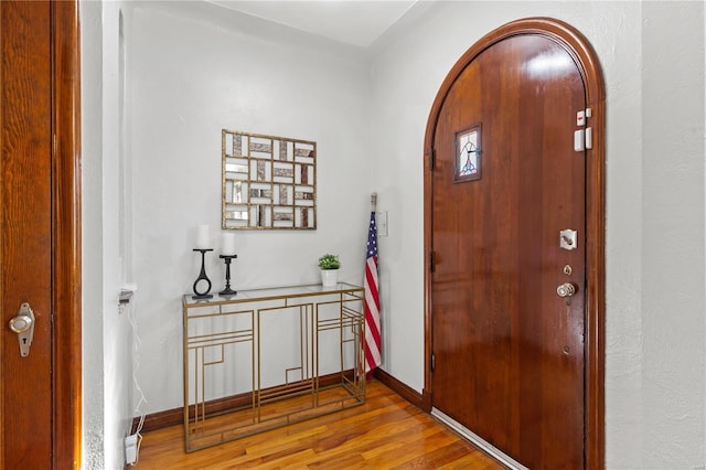 foyer featuring arched walkways, wood finished floors, and baseboards