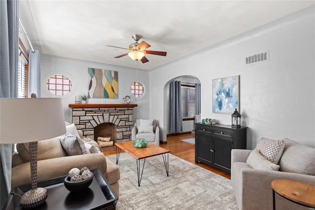 living area featuring arched walkways, ceiling fan, a fireplace, wood finished floors, and visible vents