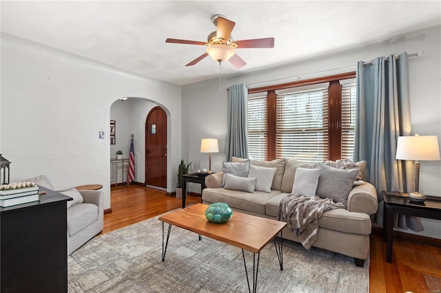 living area with arched walkways, ceiling fan, wood finished floors, and baseboards