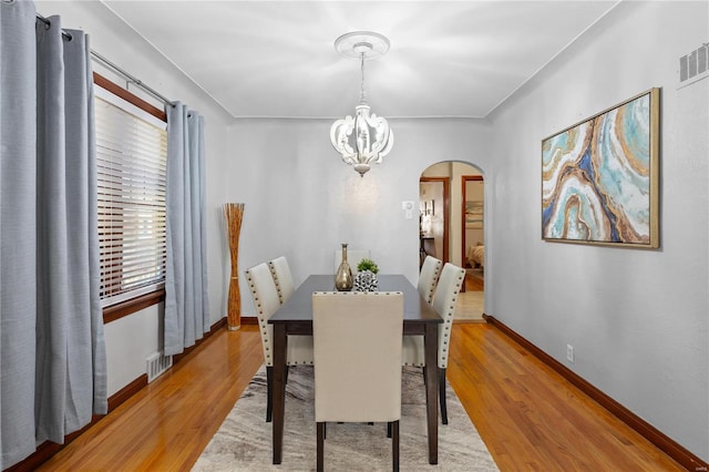 dining room featuring arched walkways, a notable chandelier, visible vents, baseboards, and light wood finished floors