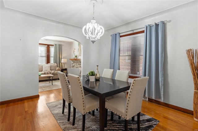 dining space featuring light wood-style floors, arched walkways, a notable chandelier, and baseboards