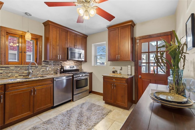 kitchen with stainless steel appliances, hanging light fixtures, backsplash, a sink, and light stone countertops