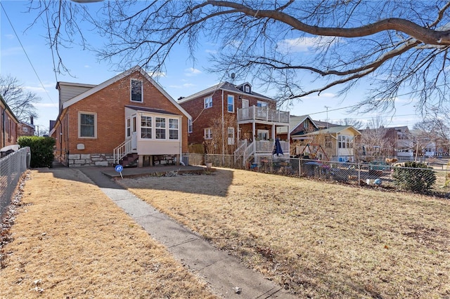 rear view of house featuring entry steps, a lawn, a fenced backyard, a residential view, and brick siding